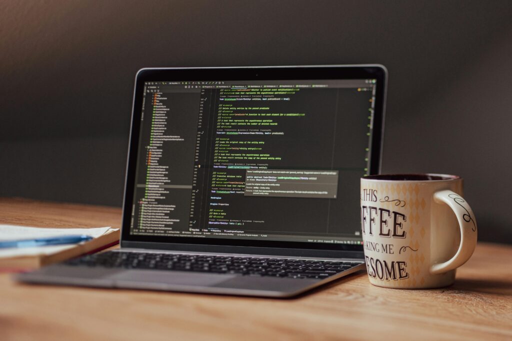 Laptop displaying code editor with coffee mug on desk, perfect for tech themes.